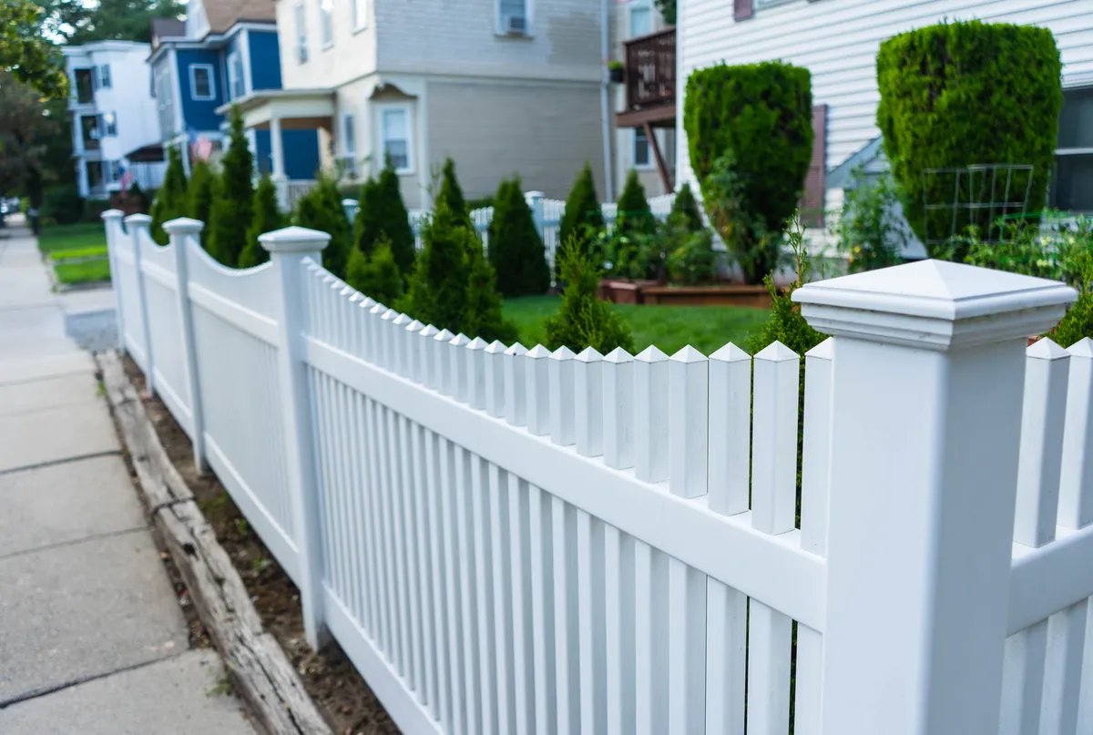 A white vinyl picket fence lining a well-manicured front yard