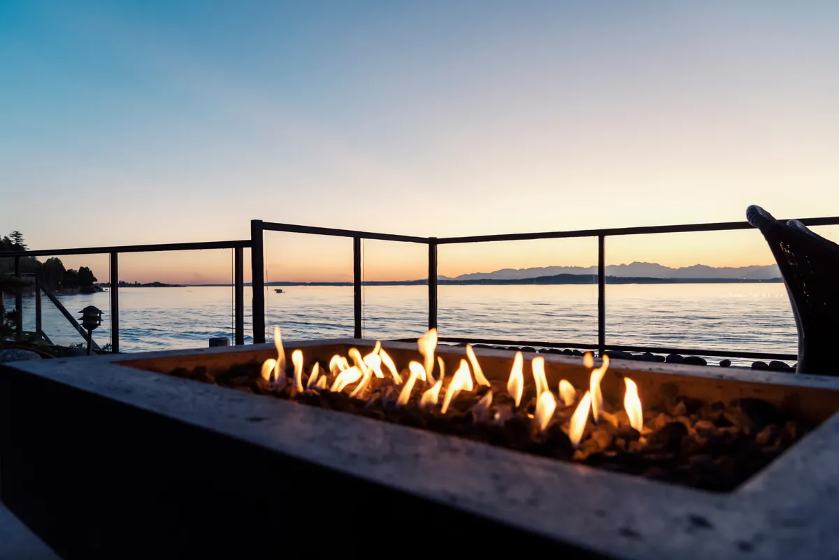 A glowing fire pit on a deck overlooking the water at sunset